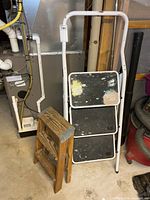 metal 3-step ladder folded next to wooden stool