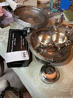 Grouping of silver-plate items on table including pedestal stands, cream and sugar, candle holder box, pewter box