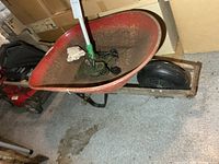 Side view of red metal wheelbarrow showing wooden handles and solid rubber tire