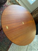 Top view of round teak coffee table showing brass hinges and wood grain