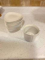 Stack of ten Bowring triangular plates beside one white ribbed mug