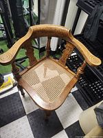 Full view of corner chair showing carved armrests, turned legs and cane seat