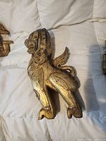 Left side view of gilded wooden Singha guardian lion showing carved detail and wear