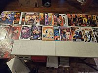 Wide view showing two rows of assorted bagged comic books laid on table