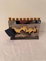 Front view showing silver backplate, gold skyline, nine candle cups, tag attached
