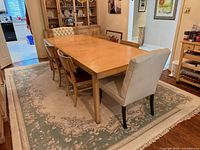 Dining table with four wood side chairs and two white host chairs around rug
