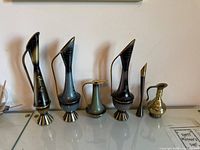 All six decorative metal vessels lined up on glass surface