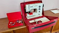 Machine in open red case with accessory box and extension table
