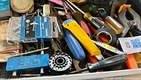 Drawer containing assorted tools and hardware including screwdrivers, utility knife, staples, clamp block, cutter wheel