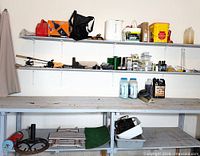 Wide view of shelves and workbench showing fuel cans, pail, hardware boxes, washer fluid, motor oil, tools, and other items