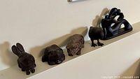 Line of four cast iron animal figurines and one black ceramic sculpture on shelf