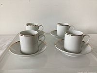 Four cups on matching saucers, side view shows gold rim accents