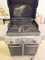Front view of Weber gas grill with lid open showing three control knobs, side shelf, cabinet doors