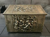 Top view showing ornate embossed figural lid and front panel detail of the brass box