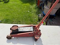 Side view of red 2-ton floor jack with handle attached, showing wear