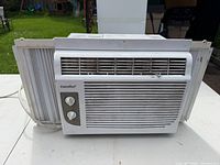 Front view of Comfee window air conditioner showing grille, dual knobs, side accordion panels
