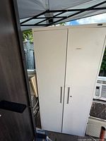 Front view of tall white metal two-door cabinet showing handles and overall condition