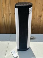 Full view of NOMA ceramic tower heater beside remote