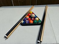 Pool balls in rack flanked by two cues