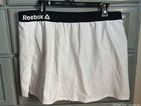 Front view of white Reebok skort hanging, black waistband visible