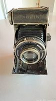 Front view of Noris folding bellows camera showing lens, bellows and nameplate
