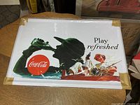 Front view of the metal Coca-Cola sign inside plastic cover