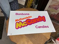 Front of white metal sign showing Bonbons, McCormicks, McCandy, Candies graphics