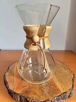 Chemex glass coffee maker on wood slice stand showing full form, collar, leather tie