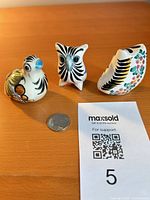 Front view of three small pottery bird figurines with size reference coin