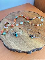 Full lot view: two cuff bracelets and bead necklace on wooden base
