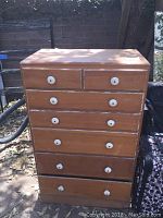 Front view of the wood dresser showing six drawers with white round knobs, natural wood finish, some wear visible.