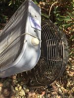 Close view of the round fan showing details of metal blades and protective cage, with a paper sticker showing price.