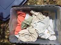 View of the plastic bin open showing assorted bedding linens inside in various neutral and pastel colors.