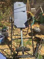 View of inversion table standing upright outdoors showing padded grey backrest, metal frame, and ankle supports