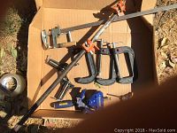 Photo showing a box with various clamps including a long 60 inch pony clamp, three Husky C clamps, an Irwin quick grip clamp, and other clamps with wooden handles.