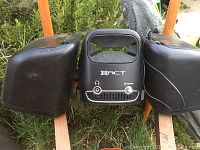 Front view of Sirius XACT Boombox showing the main speaker unit with two attached side speakers sitting outdoors on grass and wooden planks.