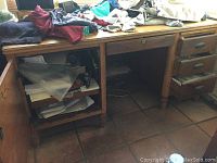 Front view of vintage solid wood desk showing open shelves and drawers on the left side, cluttered top surface