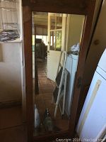 Full view of the bevelled mirror door leaning against a wall, reflecting indoor room including a door and household items.