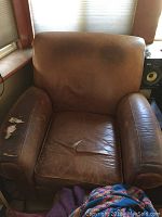 Front view of large brown leather club chair with visible wear and tears on arm and seat cushions