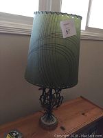 Full view of the lamp showing green shade on wooden table near window with measurement tape for scale.