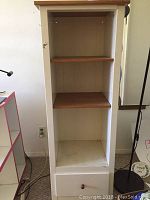 Photo of narrow shelf unit with two wooden shelves and drawer, showing age-related wear and dust.