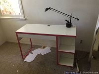 Image of the white and pink student desk with shelving and black desk lamp on top, placed near a window on carpeted floor.