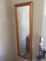 Full view of the rectangular wall mirror with wood frame leaning against wall.