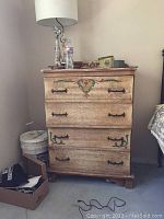 Full view of the wood dresser showing overall distressed finish and decorative painted motifs on the drawer fronts. Wrought iron handles visible on each drawer.