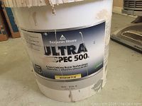 Front view of 5 gallon paint pail labeled Benjamin Moore Ultra Spec 500 interior flat with paint drips visible