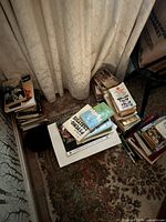 Floor view showing several stacks and a box of assorted hardcover and paperback books