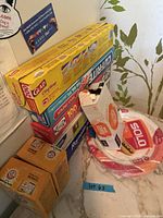 Stack showing Glad Cling Wrap, Cut-Rite wax paper, Super Cling plastic wrap, Reynolds Wrap, Solo plates, Arm & Hammer boxes