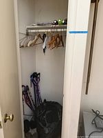 Overview of closet showing hangers on rod, flashlights on shelf, canes and duffel bag on floor