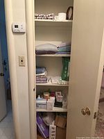 Overall view of linen closet shelves with towels, supplies, mug, wooden ring