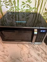 Front view of Hamilton Beach microwave showing black cabinet, stainless door trim, control panel and LED display